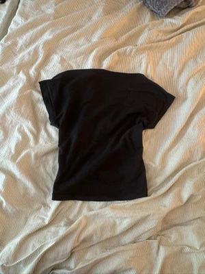Svart topp med öppen rygg - Snygg svart topp med korta ärmar och en öppen rygg. Perfekt för dig som vill ha en enkel men ändå trendig look. Materialet känns mjukt och stretchigt, troligen bomull eller polyester. Passar till många olika stilar och outfits.