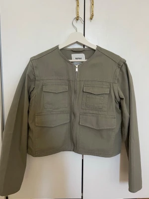 Khakigrön jacka från Monki - Helt ny oanvänd Khakigrön vår jacka från Monki med rak passform, rund halsringning och dragkedja framtill. Fyra stora fickor och avtagbara armar så den kan användas som en väst också. Storlek S