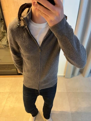 Grå stickad cardigan jacka med huva - Säljer en riktigt snygg stickad cardigan som är i mycket bra skick. 😊                    ———————————————————————————                                               📐| Storlek: L                                                           👖| Märke: Massimo Dutti                                      🔎 | Skick: Mycket bra                                            ✍🏻 | Skriv om du har några frågor