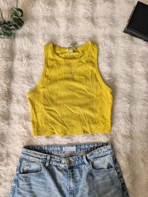 Gul ribbad croppad linnetopp - Snygg gul croppad linnetopp med ribbad struktur och rund halsringning. Perfekt för varma dagar och enkel att matcha med höga jeans eller shorts. Tidlös och fräsch färg som ger en somrig vibe.