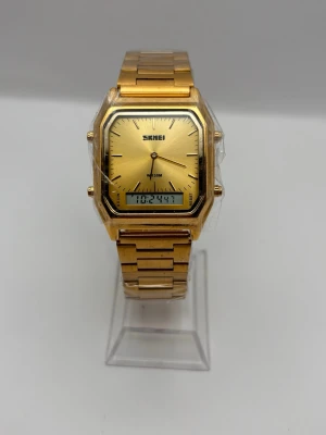 Guldfärgad digital- och analogklocka - Stilren klocka från Skmei i guldfärgad metall med både analog och digital display. Fyrkantig urtavla med minimalistisk design och länkarmband i metall. Perfekt accessoar för dig som gillar en modern och klassisk look.