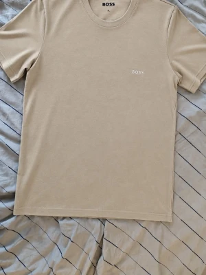 Beige t-shirt från BOSS - Snygg beige t-shirt från BOSS med diskret logga på bröstet. Klassisk rund halsringning och korta ärmar. Perfekt basplagg som passar till det mesta och är riktigt enkel att matcha.