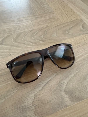 Ray-Ban Boyfriend 4147 - Snygga solglasögon från Ray-Ban med brunmelerad båge och stora, fyrkantiga glas. Klassisk modell som ger en cool vibe och passar till många stilar. Ljusbruna tonade glas och diskret Ray-Ban-logga på linsen. Perfekta för soliga dagar.