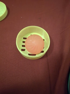 Rund rosa tvål med tvålfat - En rund, rosa tvål med spiralformat mönster säljes tillsammans med ett gult tvålfat i plast. Perfekt för badrum eller resor. Tvålen har en fräsch look och tvålfatet har ventilationshål i botten för att hålla tvålen torr.
