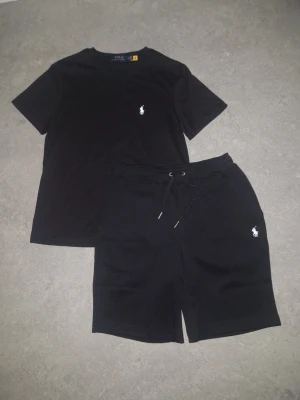 Svart t-shirt från Polo Ralph Lauren - Säljer en svart t-shirt från Polo Ralph Lauren med den klassiska vita loggan broderad på bröstet. T-shirten har rund hals och korta ärmar, perfekt för en clean och stilren look. Materialet är mjukt och skönt bomull.