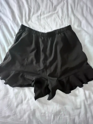 Svarta volangshorts från H&M - Säljer ett par svarta shorts från H&M med volangkant nedtill. Väldigt sköna o är likt en kjol💞.