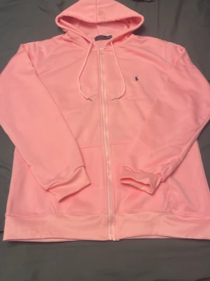 Rosa hoodie från Polo Ralph Lauren - Snygg rosa hoodie med dragkedja från Polo Ralph Lauren. Klassisk huva med dragsko, broderad logga på bröstet och mjukt material. Perfekt för en avslappnad och trendig look.
