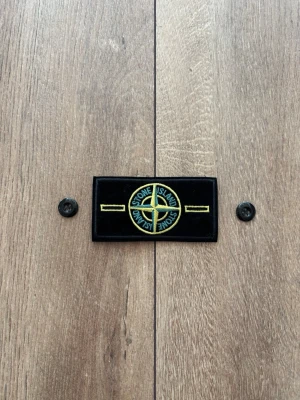 Stone Island Patch / Badge – Gul/grön klassisk design & knappar - Säljer en klassisk Stone Island-badge med tillhörande originalknappar, precis som visas i bilden. Patchen är helt ny, aldrig använd och i perfekt skick. Perfekt som reservdel till din Stone Island-jacka eller tröja. 