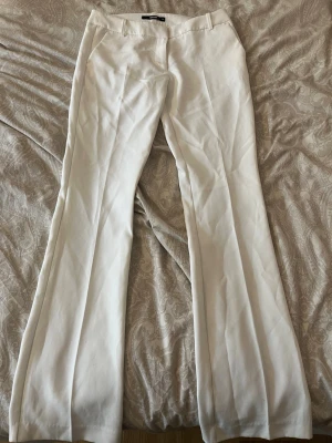 Vita vida kostymbyxor - Snygga vita kostymbyxor med pressveck och utsvängda ben. Byxorna har fickor fram och hällor för skärp. Perfekta för en clean och stilren look. Materialet ser ut att vara en mjuk och lätt blandning, vilket ger en skön känsla. ALDRIG ANVÄNDA🌸🌸