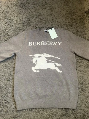 Burberry tröja - Snygg grå stickad tröja från Burberry med vit logotyp och ikonisk riddare framtill. De är i bra skicka och är helt ny