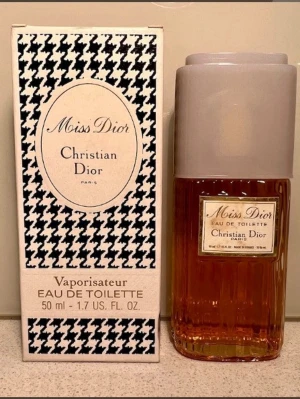 Miss Dior Eau de Toilette 50 ml - Miss Dior Eau de Toilette från Christian Dior i en elegant glasflaska med ljusbeige lock. Flaskan rymmer 50 ml och har en klassisk etikett framtill. Förpackningen har ett svartvitt mönster och stilren design.