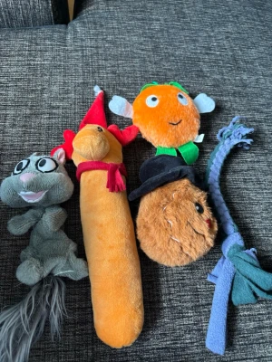 Fem olika mjukisdjur och leksaker - Säljer ett gäng roliga mjukisdjur och leksaker i olika färger och former. Här finns bland annat en grå ekorre, en lång orange korv med röd hatt och halsduk, en rund orange figur med vingar, en brun boll med svart hatt och en blå flätad leksak. Perfekt för lek eller dekoration!