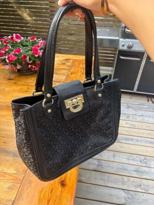 Svart handväska från DKNY - Snygg svart handväska från DKNY med rymlig insida med fack. Väskan är i mycket bra skick! Väskan är ca 34 cm bred,  27 cm hög (ej medräknad hantagen) ca 13 cm djup 💕