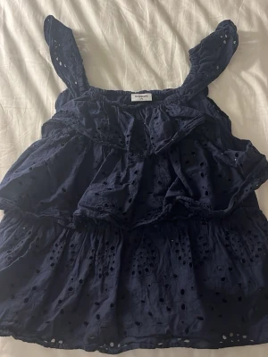 Mörkblå volangig linnetopp - Supersöt mörkblå linnetopp med volanger och broderade hål från Kappahl. Toppen har breda axelband och ett luftigt, flowy material som passar perfekt till sommaren. Perfekt att styla med jeans eller kjol för en chill look.