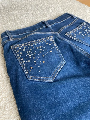 Blå jeans med paljetter från Lindex - Snygga blå bootcut jeans från Lindex i storlek 152. Med paljetter på fickorna, low waist