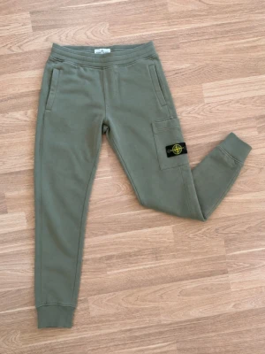 Stone Island Junior cargobyxor / sweatpants 🫒 - Snygga olivgröna Stone Island Junior-byxor med den klassiska avtagbara Stone Island-badgen på benfickan. • Stone Island Junior • Olivgrön / khakigrön • Cargo-/joggermodell • Sidofickor + cargoficka och bakficka • Ribbad midja och muddar vid bensluten • Certilogo finns för autenticitetskontroll • Fint begagnat skick utan defekter! Riktigt snygg och stilren modell som är lätt att matcha. Skickar gärna fler bilder eller mått vid intresse 📦 Storlek 156 men passar ca xs i vuxenstorlek!