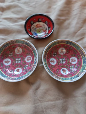 Retro kinesiska Mun Shou skålar Jingdezhen + Handmålad turkisk skål – 3 delar. - Säljer ett fint och färgglatt set med tre mindre skålar/dipskålar: 2 st kinesiska porslinsskålar (Mun Shou / Wan Shou): Klassiskt emaljerat mönster i rosa och multikolor med tecknet för "Långt liv". Stämplade i botten (*Jingdezhen / Made in China*). Retro från ca 1970/80-tal. 1 st mindre keramikskål:** Handmålad i turkisk stil med vackert mönster och fina detaljer i relief. Material: Porslin och keramik * Skick: Mycket fint skick, hela och rena utan nagg (se bilder för egen bedömning).