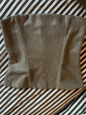 Glittrig svart korsett-topp - Säljer en snygg svart korsett-topp från Zara ,täckt med glittriga stenar som ger ett riktigt statement. Toppen är axelbandslös och har en tight passform som framhäver midjan. Perfekt för dig som vill sticka ut och glänsa.  Nypris 500kr