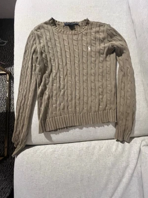 Klassisk grön kabelstickad tröja från Ralph Lauren 🌟💗 - Säljer en tidlös "Cable-Knit" i en jättefin grön färg. Perfekt basplagg till garderoben som passar till både jeans och finbyxor. Den ikoniska polospelaren är broderad på bröstet i vitt. Gjord av 100% bomull! Rökfritt hem, pris kan diskuteras och hör gärna av dig om du har frågor!💗🌟