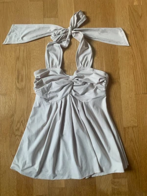 Ny Ljusgrå babydoll topp  - Supersnygg ljusgrå babydoll topp med knytband i nacken och draperad byst. Toppen har en lätt utsvängd passform och mjukt, stretchigt tyg som ger en skön känsla. Perfekt till sommaren och för dig som gillar en trendig look. Vet tyvärr inte märket på den men ser ut som 2000s look