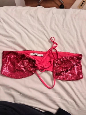 Rosa paljettbikinitopp från NA-KD - Snygg rosa bikinitopp från NA-KD med glittriga paljetter och snörning i ryggen. Perfekt för dig som vill sticka ut på stranden eller poolpartyt. Bandeau-modell med tunna band som knyts i ryggen.
