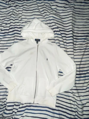 Ralph lauren - Riktigt snygg vit zip up hoodie från Polo Ralph Lauren.Storleken är 14-16 men passar även xs.Den sitter väldigt bra på kroppen och är lätt att styla.Tillverkad i mjukt bomullsmaterial som känns skönt mot huden. Självklart äkta ✅och hör av i dm om frågor