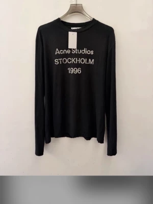 Svart långärmad topp Acne Studios - Svart långärmad topp från Acne Studios med tryck 'Acne Studios STOCKHOLM 1996' framtill. Tunn och mjuk kvalitet med rund halsringning. Perfekt för en clean och stilren look.