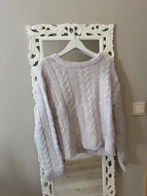 Ljusgrå kabelstickad tröja - Mysig ljusgrå kabelstickad tröja med rund hals och långa ärmar. Tröjan har ett klassiskt flätmönster framtill och är tillverkad i ett mjukt material som passar perfekt för kyligare dagar. Enkel och stilren design som är lätt att matcha.