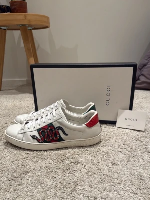 Gucci Ace - Säljer nu dessa riktigt snygga och eftertraktade Gucci Ace skor i storlek UK 9, vilket motsvarar 43 i EU. Nypris: 9000 kr. Skorna är i mycket bra skick. Endast en liten defekt på ena hälen och lite smått normalt slitage vid insida häl. I allmänhet är dem mycket väl omhändertagna. Skorna är helt äkta och köpta från Fashionstore. Skorna skickas med box och certifikat. Vid fler frågor kring äkthet och äkthetsbevis, eller något annat om skorna, hör av dig!