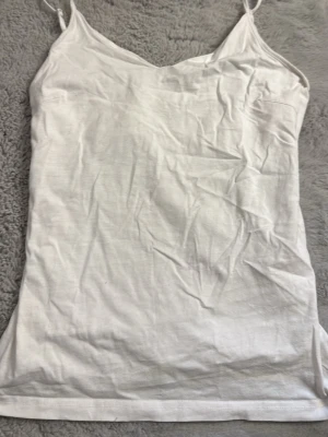 Vit linnetopp från 157 - Säljer en enkel och stilren vit linnetopp från 157 med tunna axelband och v-ringad hals. Tillverkad i mjuk bomull med lite stretch för skön passform. Perfekt att matcha med jeans eller kjol.