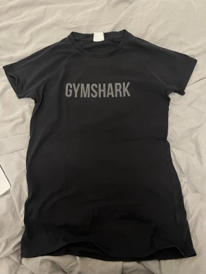 Svart Gymshark t-shirt - Svart t-shirt från Gymshark med tryckt logga på bröstet. Modellen har korta ärmar och rund halsringning. Perfekt för träning eller gymmet, tillverkad i ett stretchigt och mjukt material som andas.
