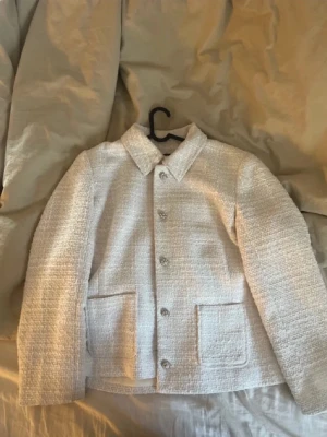Vit kavaj-kappa - Stilren vit kavaj-kappa i tweedliknande material med klassisk krage och dekorativa knappar framtill. Kappan har två stora fickor framtill och raka ärmar. Perfekt för dig som gillar en chic och enkel look. Så otroligt classy och snygg!🍁🍂