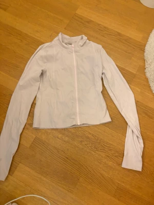 Ljusrosa träningsjacka  - Snygg ljusrosa vindjacka med hög krage och hel dragkedja framtill. Jackan har en clean och minimalistisk look med långärmad passform och lätt material, perfekt för lager på lager under vår och sommar.