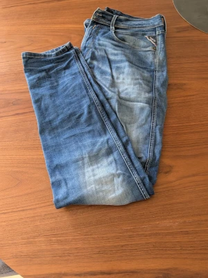 Blå jeans med slitningar - Säljer ett par klassiska blå jeans med snygga slitningar och tvättade detaljer. Jeansen har fem fickor, normal midja och raka ben. Perfekta för en avslappnad och trendig stil.