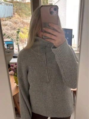 Grå ribbstickad polotröja - Mysig grå ribbstickad polotröja med dragkedja i halsen och långa ärmar. Tröjan har en avslappnad passform och är perfekt för kyliga dagar. Kommer tyvärr aldrig till användning 💕💕Skulle säga att passformen passar även S och M, inga defekter!