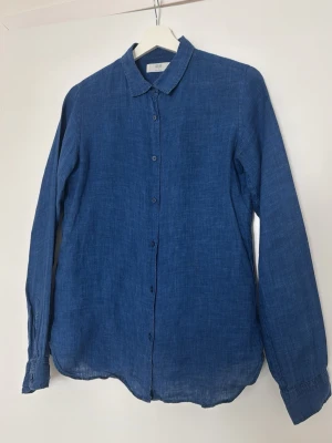 Blå Uniqlo linneskjorta - Snygg blå skjorta i linne med klassisk krage och knäppning framtill. Storlek S upplevs mer som XS.