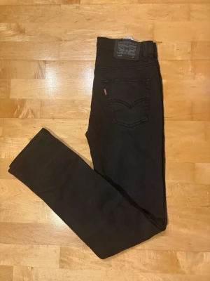 Levis med slitage - Säljer ett par svarta slim fit jeans med slitningar från Levi's med klassisk femficksdesign och röd logotagg på bakfickan. Jeansen har normal midja och raka ben. Perfekta till en avslappnad streetstil och funkar året runt. 