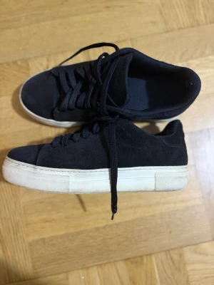 Selected homme låga sneakers - Stilrena svarta sneakers i mocka med vita, tjocka sulor och svarta skosnören. Klassisk låg modell som passar till det mesta och ger en clean look. Perfekta för dig som gillar enkel och tidlös stil.