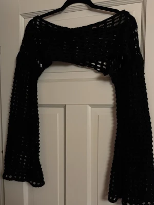 Svart virkad bolero med vida ärmar - Säljer en svart virkad bolero med riktigt vida ärmar och ett öppet nätmönster. Perfekt att slänga över ett linne eller klänning för en cool lager-på-lager-look. Materialet är mjukt och stretchigt, vilket gör den bekväm och enkel att styla.