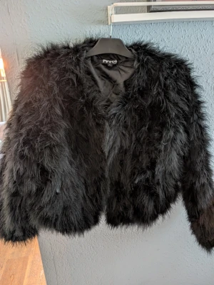 Svart fluffig pälsjacka - Säljer en svart, superfluffig pälsjacka med mjukt foder. Jackan har en kortare modell som ger en lyxig och trendig look. Perfekt för dig som vill sticka ut och hålla dig varm under vintern. Stängs framtill och har långa ärmar. Se bilder för material