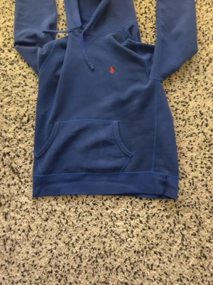 Mörkblå hoodie från Polo Ralph Lauren - Snygg mörkblå hoodie från Polo Ralph Lauren med klassisk huva och liten röd logga på bröstet. Tillverkad i mjukt bomullsmaterial som känns skönt mot huden. Perfekt för dig som vill ha en stilren och bekväm hoodie.