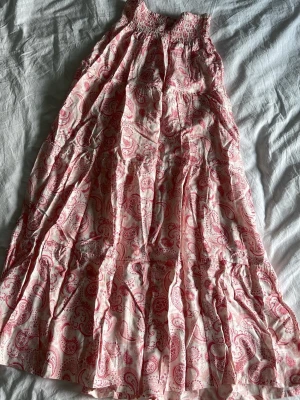 Rosa paisleymönstrad långklänning H&M - Långklänning från H&M i vitt och rosa med paisleymönster. Klänningen har smock upptill och ett luftigt fall, perfekt för varma dagar. Tillverkad i mjuk bomull och har en avslappnad passform.