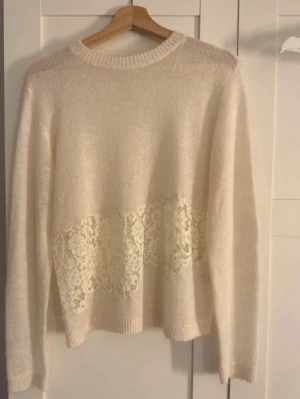 Trendig Vit stickad tröja med spetsdetalj - Säljer en mjuk vit stickad tröja med rund hals och lång ärm. Tröjan har en bred spetsdetalj i midjehöjd som ger en romantisk touch. Perfekt för dig som gillar en feminin och stilren look.