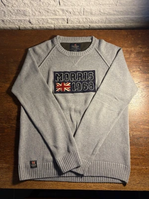 Morris grå stickad  - Snygg grå stickad tröja från Morris med broderad Union Jack-flagga och texten 'Morris 1968' på bröstet. Hör av dig vid eventuella frågor!