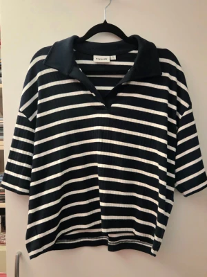 Marinblå och vit randig top - Marinblå och vit randig t-shirt med bred krage och trekvartsärm. Tröjan har en loose passform och är gjord i ett ribbat material som ger en avslappnad och trendig look.