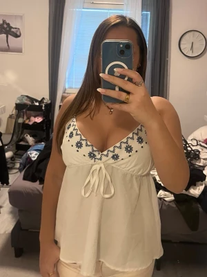 Babydoll top - Vit linnetopp/ babydoll topp med blå broderade blommor längs urringningen och knyt framtill. Används ett par gånger men inga tecken på användning - alltså inga fel eller skavanker. Från shein men klippt av lappen då den var jobbig