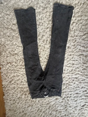 Svarta bootcut jeans med rå kant - Säljer ett par svarta bootcut jeans med råa kanter nertill. Jeansen har klassisk femficksdesign och dekorativa sömmar på bakfickorna. Tillverkade i stretchigt denimtyg som sitter snyggt och bekvämt. Perfekta för en avslappnad och trendig look.