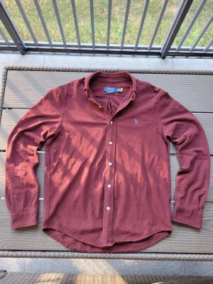Mörkröd skjorta från Polo Ralph Lauren - Säljer en mörkröd långärmad skjorta från Polo Ralph Lauren med klassisk krage och knappar framtill. Skjortan har en broderad logga på bröstet och är tillverkad i mjuk bomull. Perfekt för en stilren look.