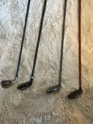 Fyra olika golfklubbor - Säljer fyra golfklubbor i olika modeller och färger. Klubborna har skaft i svart och rött samt klubbhuvuden i metall. Perfekt för dig som vill komplettera din golfutrustning eller testa olika typer av slag på banan.