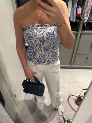 Blåvit axelbandslös tubtopp - Säljer en snygg axelbandslös tubtopp i blått och vitt med blommigt mönster. Toppen har bandeau-modell och är perfekt för sommarens varma dagar. Materialet känns mjukt och följsamt mot huden.